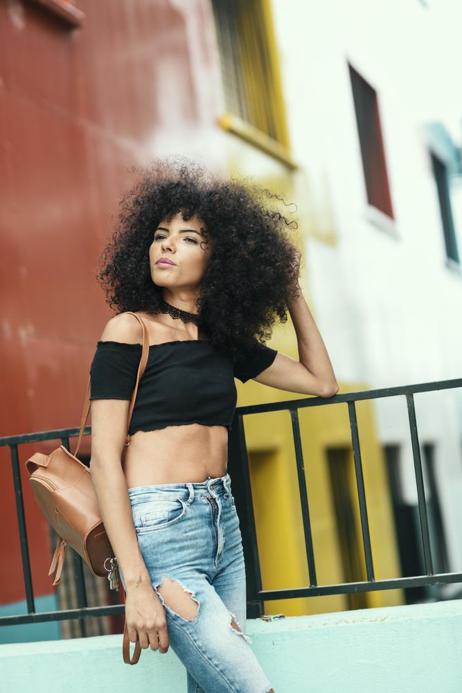 Young woman with afro hair looking around near a modern colorful building, vertical