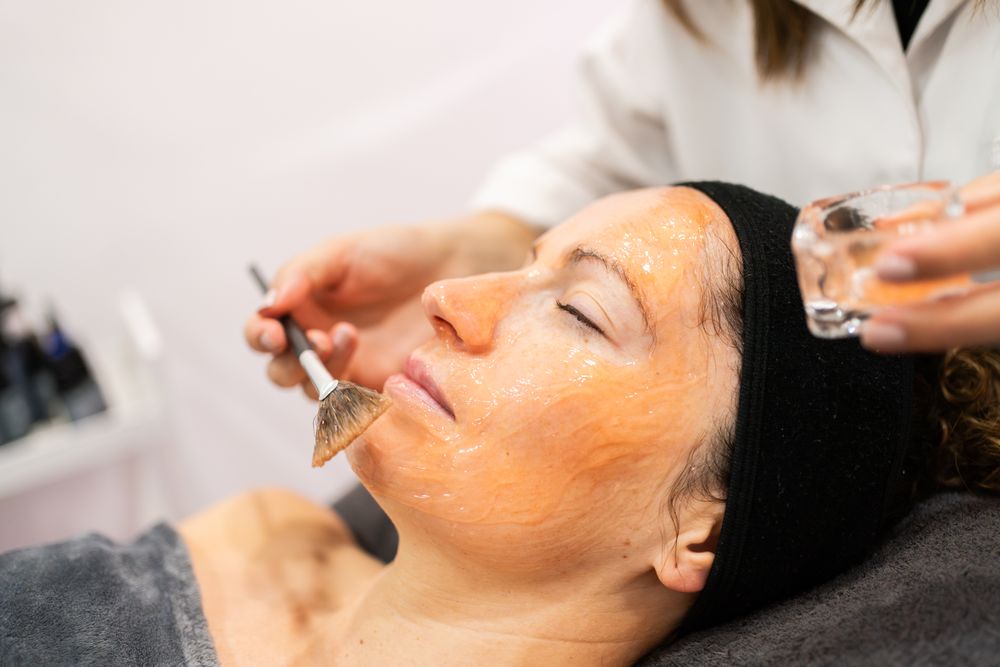 Side view of cosmetologist brushing product on client's chin