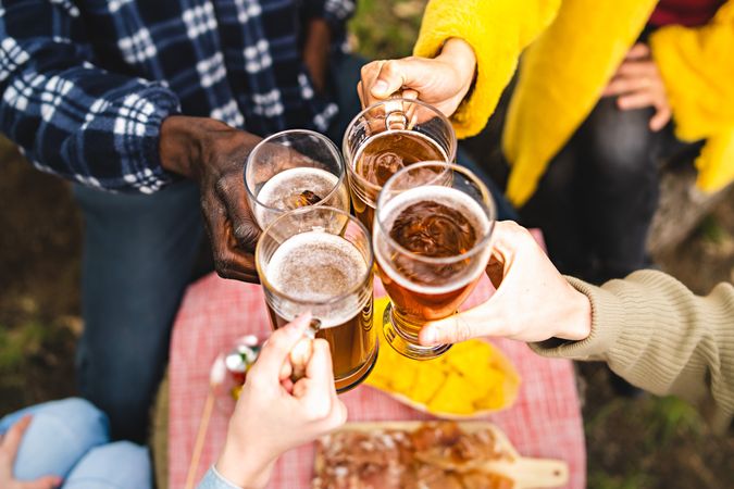 Closeup of multi-ethnic hands holding beer mugs and toasting together outdoors