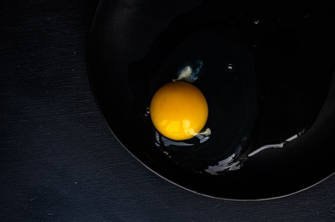 Cracked raw egg on dark surface