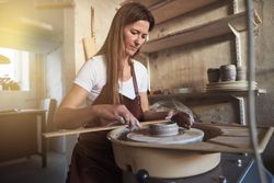Woman in leather apron molding ceramics on a wheel with a ruler