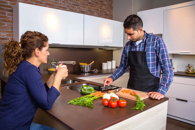 Man checking digital tablet for instructions as he prepares dinner with wife looking on