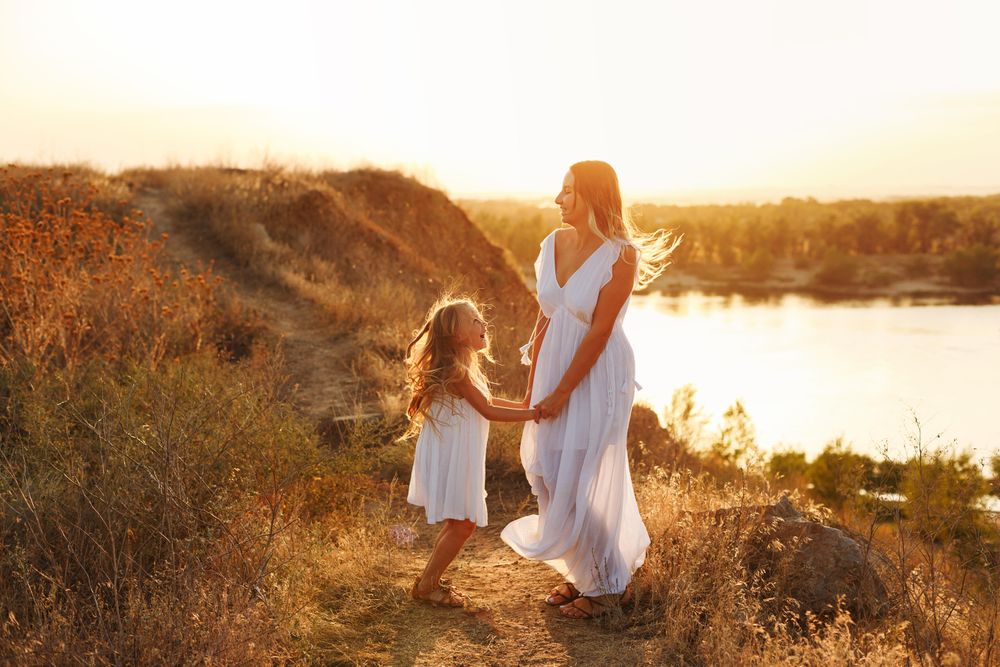 Female child in dress dancing with woman by river at dusk