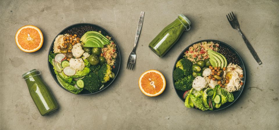 Two vegetarian bowls, with smoothie, orange halves, silverware