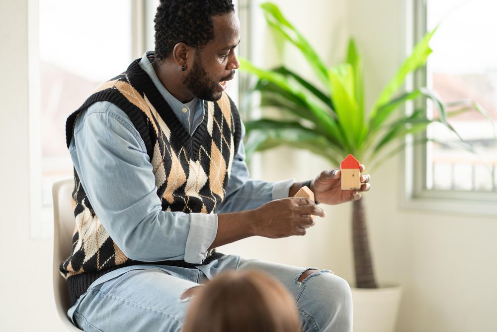 Male teacher seated in class with model home in his hand