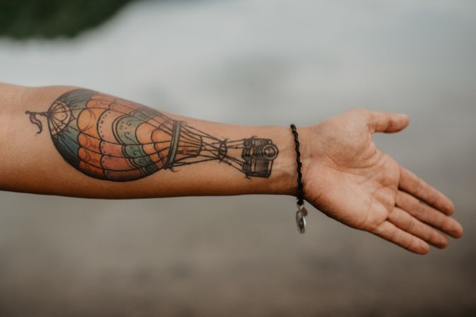 Crop tattooed arm over calm water