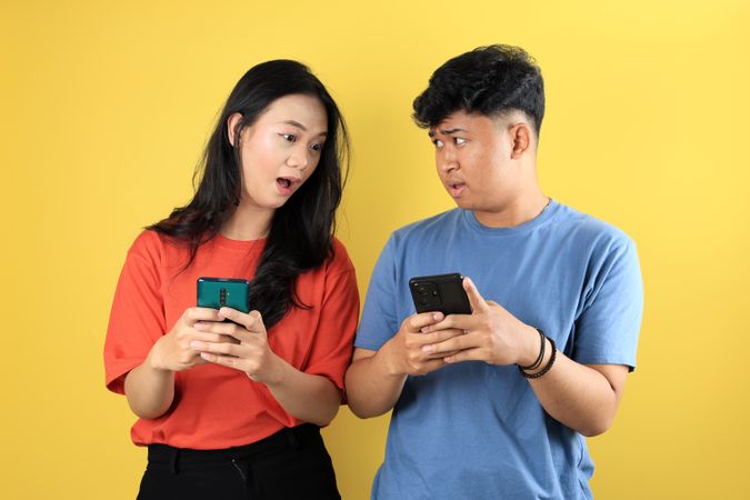 Young Asian Couple Standiing While Holding Mobile Phone, Shocked Face.