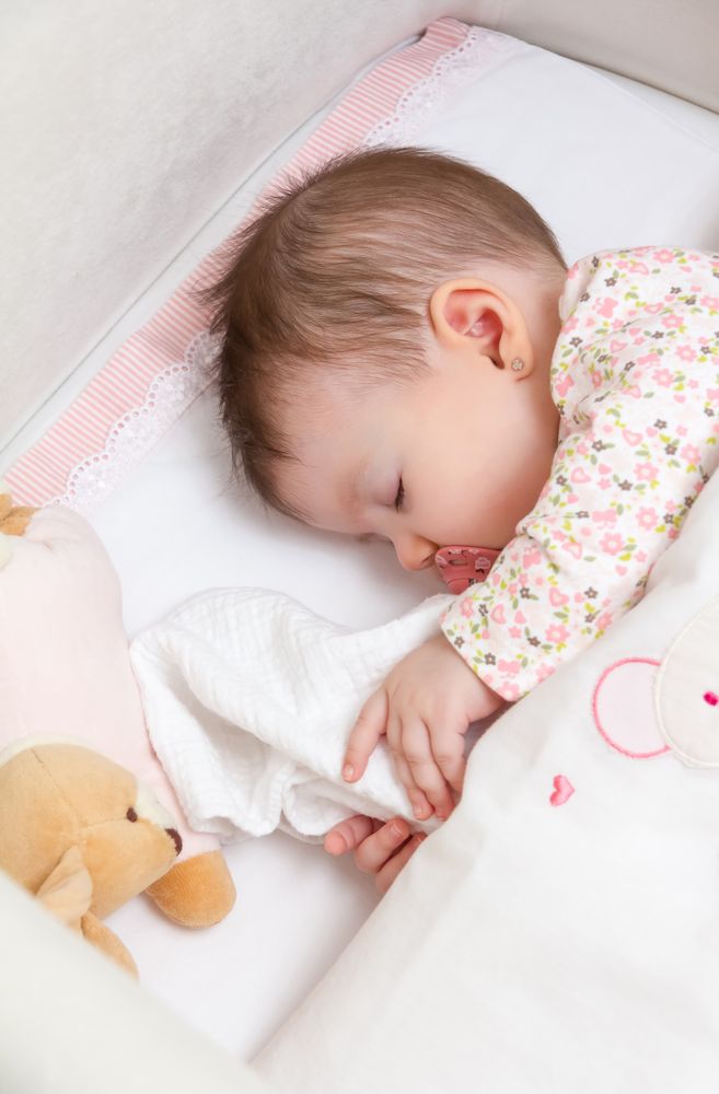 Baby girl sleeping in a cot with pacifier and toy