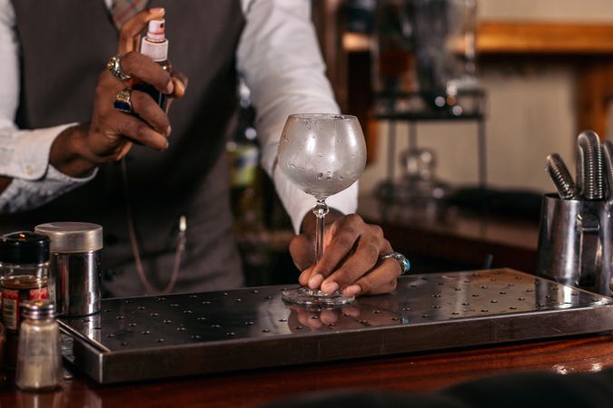stylish Black bartender in a hat serving a cocktail decorated with garnish. He is scenting the cup