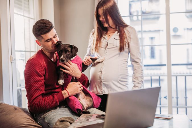 Young couple expecting baby having fun with dog at home