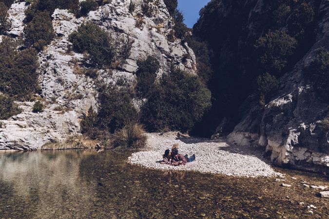Positive woman and man resting and kissing on stone shore near river