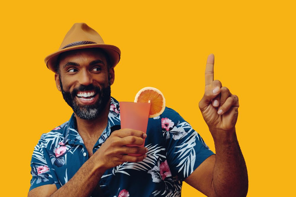 Happy male giving pointing up while wearing colorful shirt with yellow background