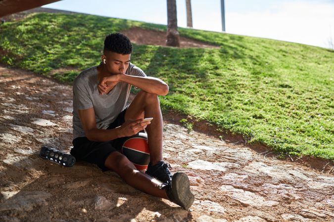 Hispanic sportsman with ball browsing smartphone on street