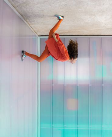 Upside photo of woman in orange casual outfit leaning her head back with one foot on wall