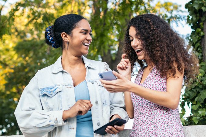 Black Latina friends using a smartphone in the park.
