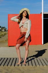 A long hair fashion model with a hat at the beach in front of a red wall