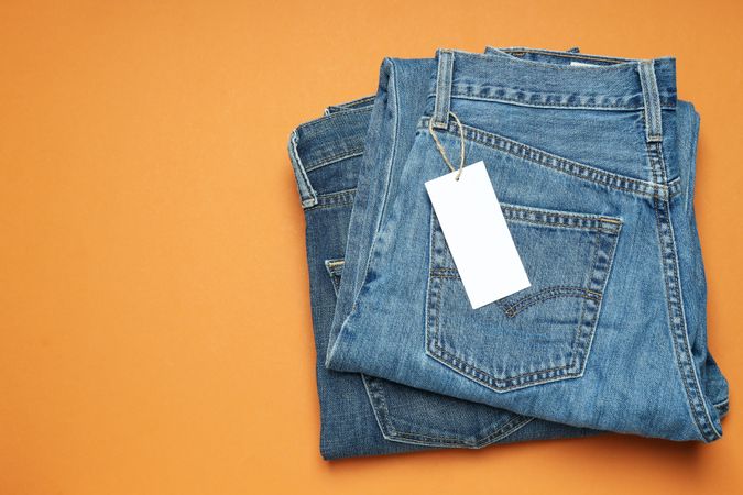 Folded jeans with a tag on an orange background