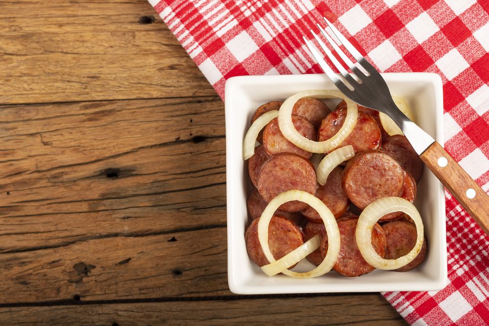 Sliced calabrese sausage with onion on wooden background.