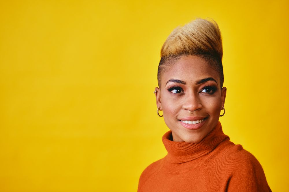 Studio shot of confident smiling Black woman posing with short blonde hair in orange sweater