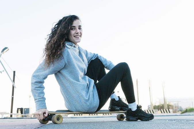 Teenage girl sitting on a longboard looking at camera while smiling