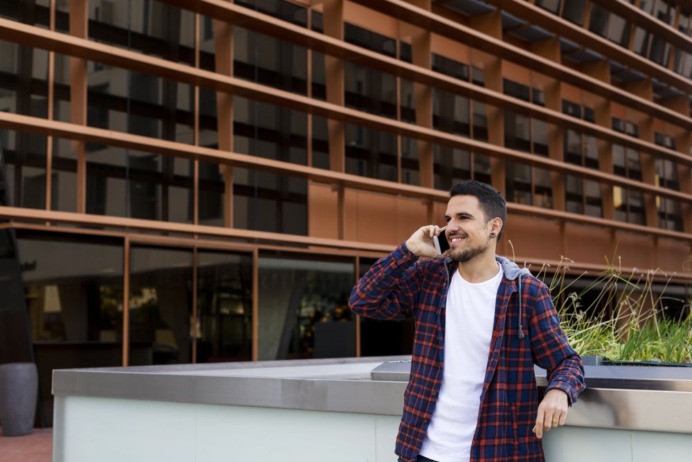 Young man smiling and talking on mobile phone outside