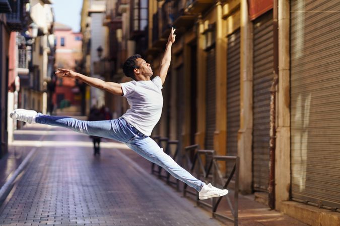 Supple male dancer in jeans and t-shirt leaping on an empty European street