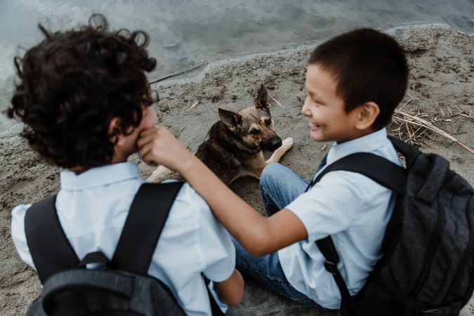 Happy boys in school uniform sitting with backpack and dog