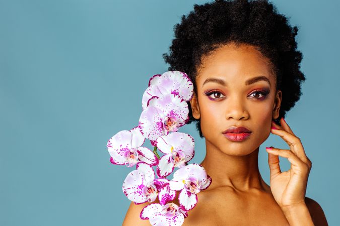 Studio beauty shot of a Black woman with purple flowers in blue space