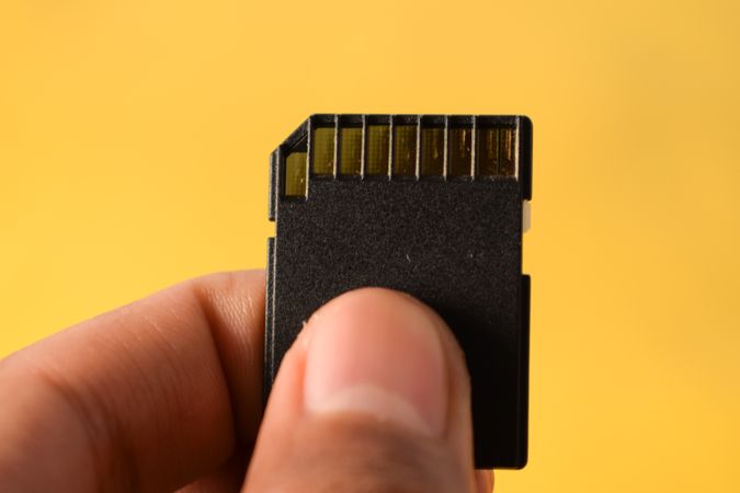 Close up of SD card in hand with yellow background and copy space