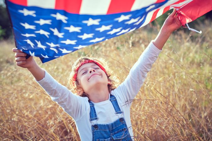 Preteen boy waving American flag in field
