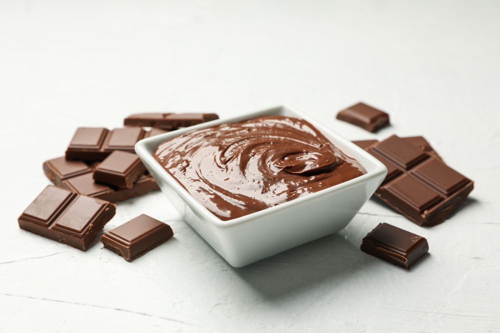Bowl with chocolate and chocolate pieces on light background