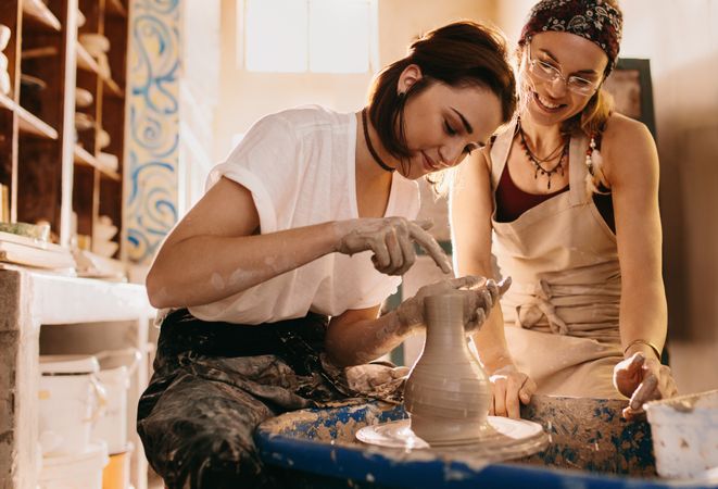 Two women at a pottery workshop making clay pots in sunny studio