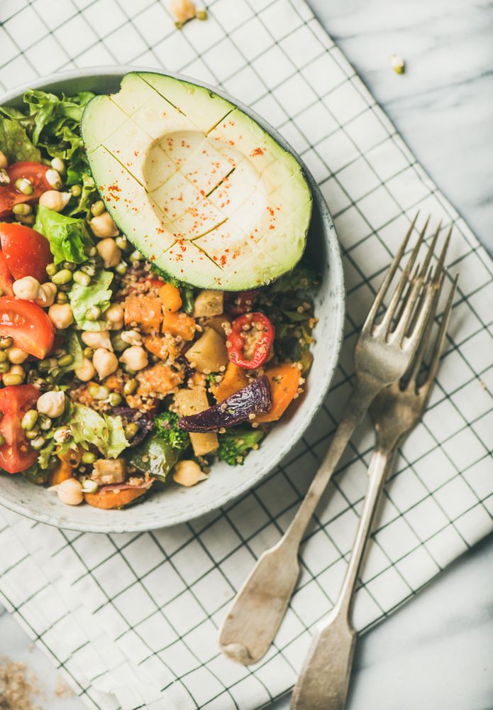 Healthy vegan lunch bowl with avocado, sprouted grains, vegetables, with forks on checkered napkin