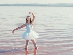Ballerina in swimsuit with tutu performing classical position in water