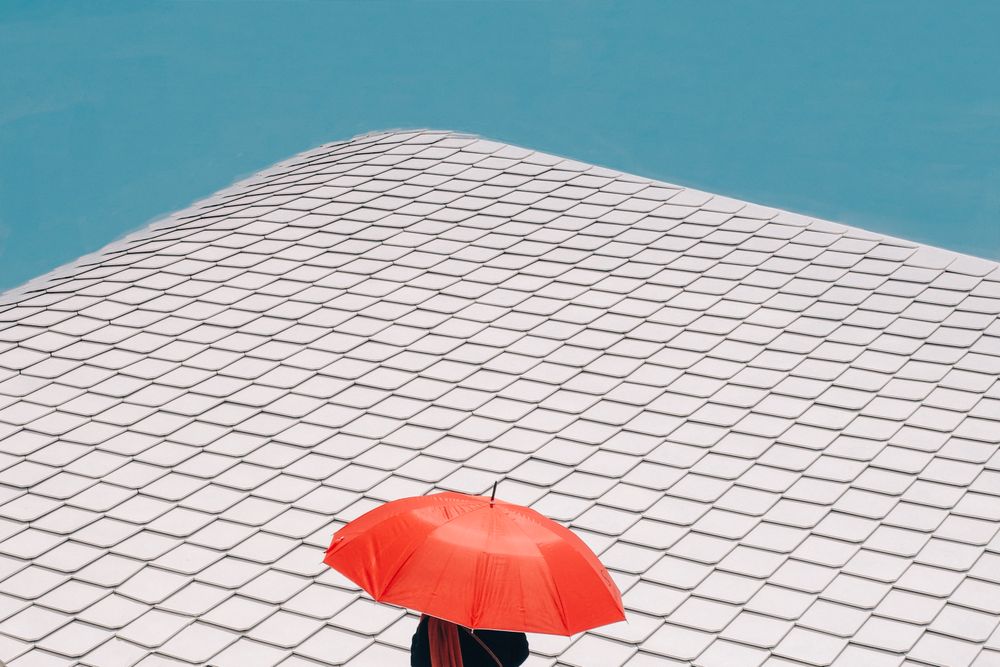 Person under red umbrella in urban setting with blue sky