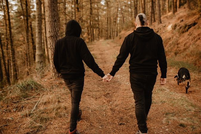 Men holding hands and walking in forest with dog