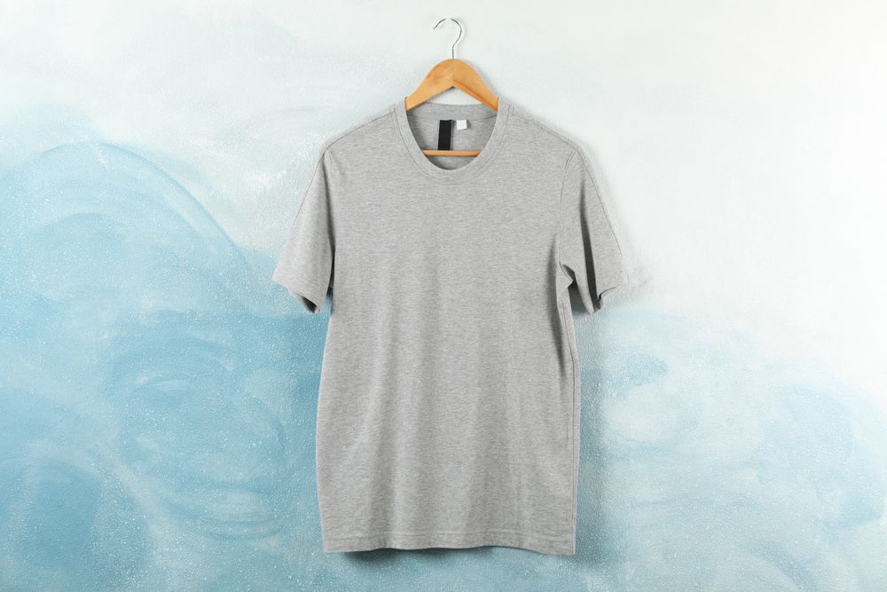 Hanger with blank gray t-shirt on blue background, space for text