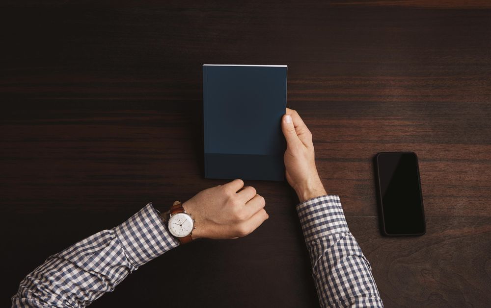 Arms in plaid shirt checking watch with on one hand, and holding book