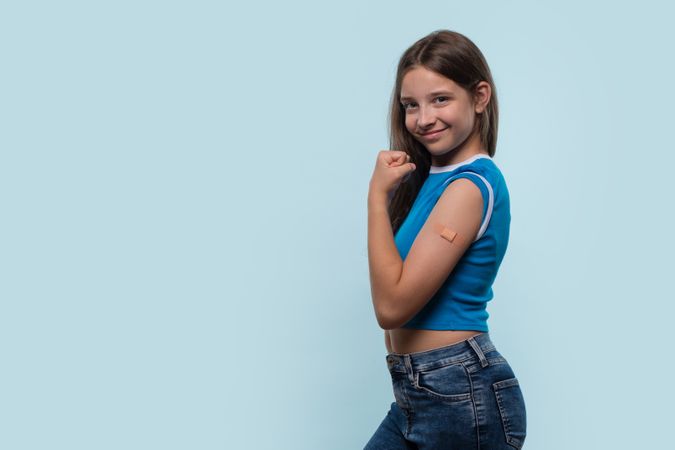 Girl flexing arm and showing bandage after vaccination