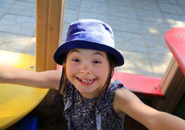Portrait of little girl on the playground in a blue hat looking up at camera and smiling