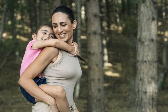 Happy mother and daughter hugging during a piggyback ride in the forest, with copy space.