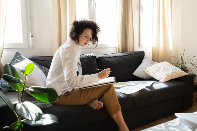 Woman writing on paper on sofa in room