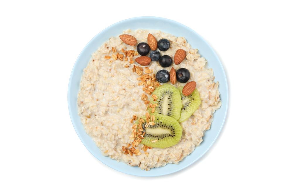 Bowl with oatmeal porridge and ingredients isolated on plain background