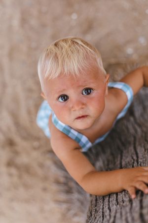 Top view of a blonde baby on the beach.to a tree
