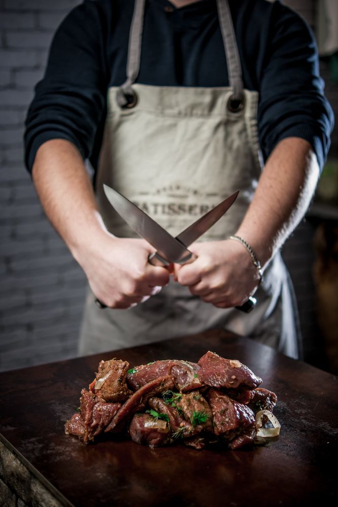 Man holding two stainless steel knives over meat slices