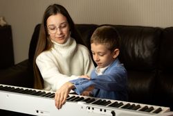 Teen girl teaching young boy to play the piano.