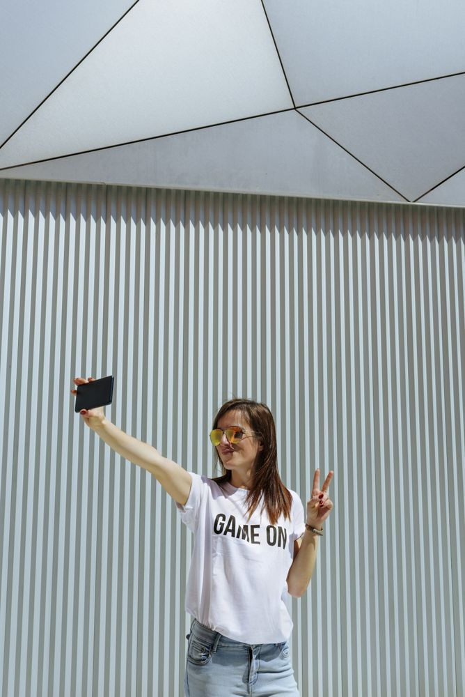 Cheerful woman taking selfie and posing near modern wall
