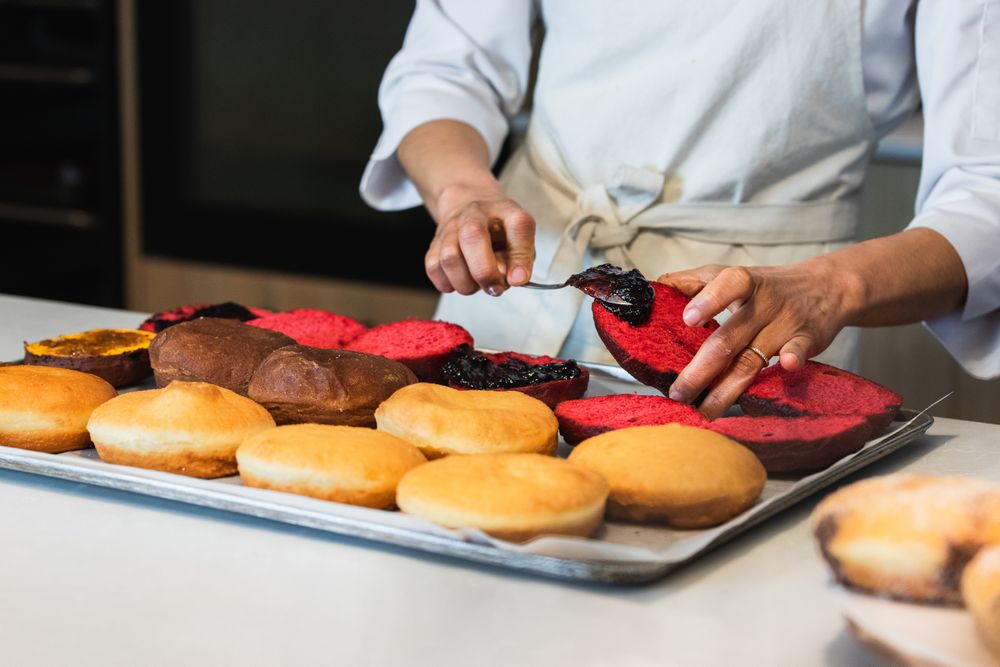 Crop cook adding jam on sponge cakes in bakehouse