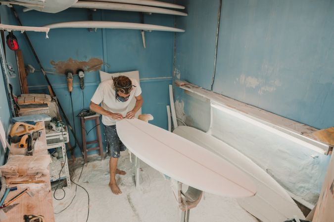 Man in respirator polishing surf board in workshop