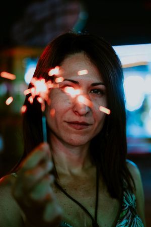 Woman holding sparkler on fairground in evening